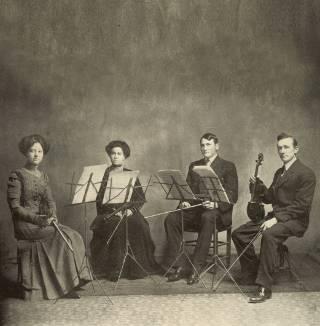 Four student musicians from 1911 pose for a photo with instruments