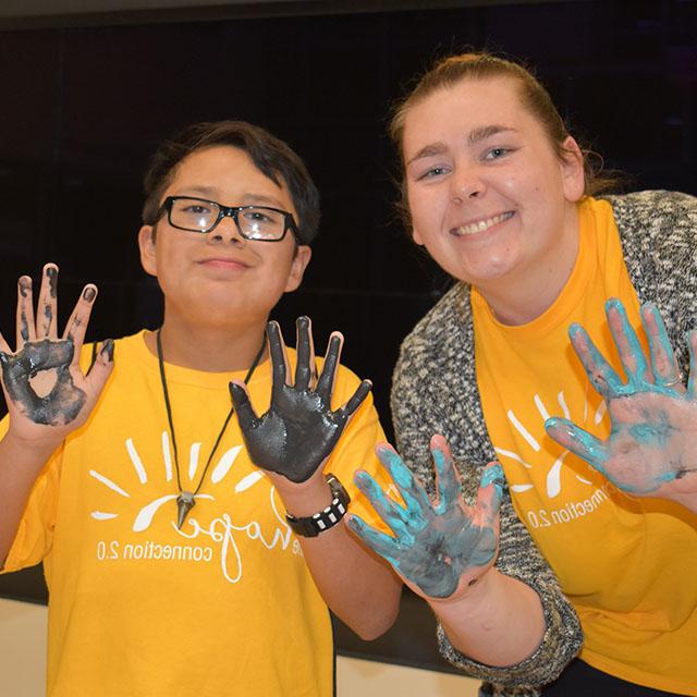 一名教师和一名年轻学生展示了他们绘画活动的证据，手掌上涂满了指画颜料